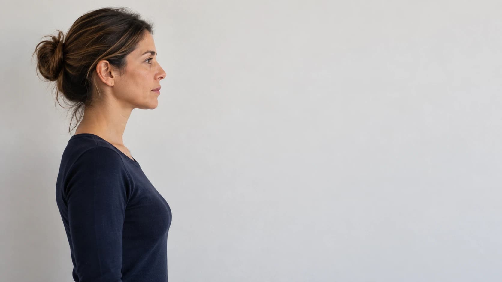 Mulher de perfil contra uma parede clara, de ombros direitos e lábios fechados, numa avaliação da postura e do perfil facial